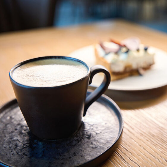 Kaffe in einer schwarzen Tasse und einer Croissant daneben