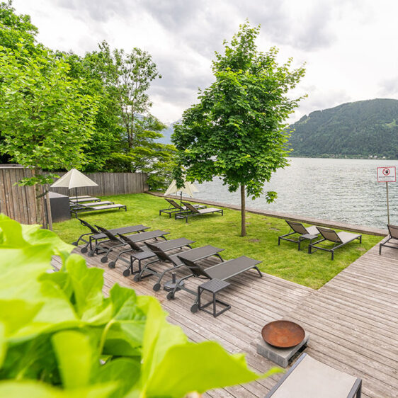 Liegestühle auf einem Steg und auf einer Wiese direkt am See