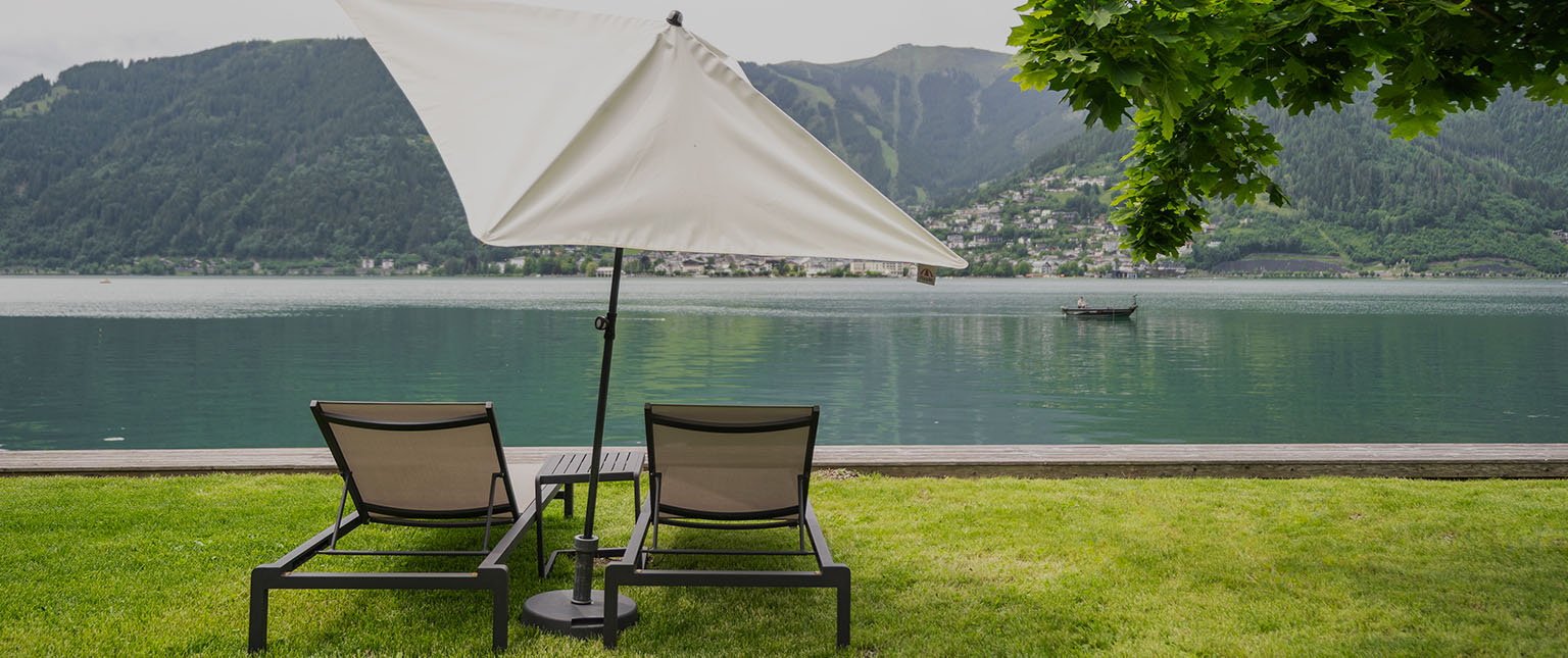 Liegestühle mit Sonnenschirm direkt vor einem See