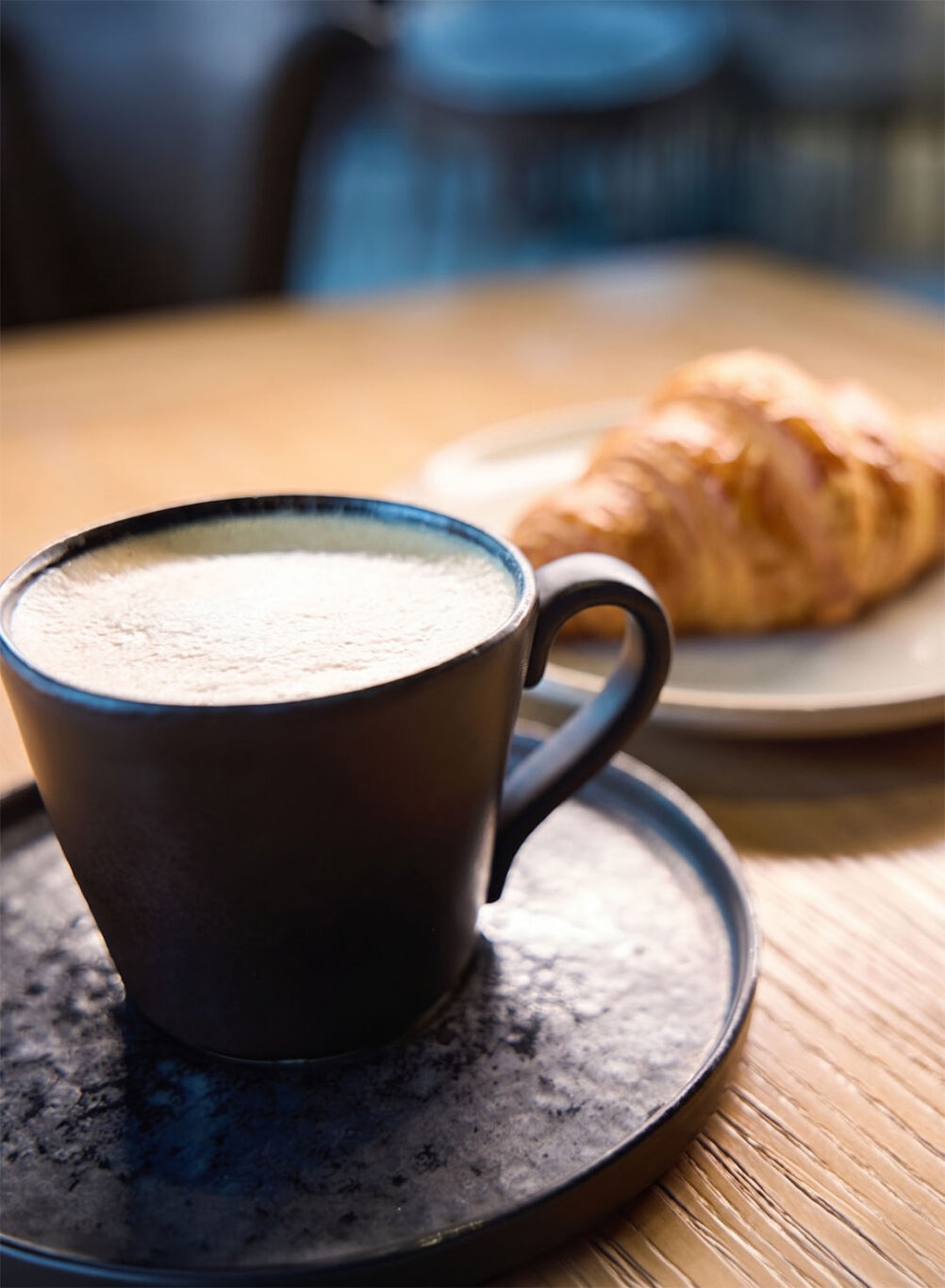 Kaffe in einer schwarzen Tasse und einer Croissant daneben