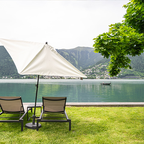 Liegestühle mit Sonnenschirm direkt vor einem See